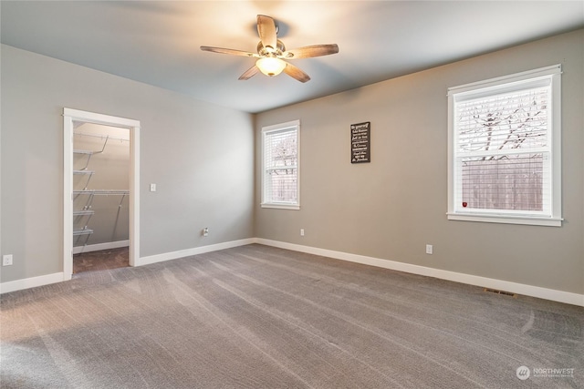 unfurnished bedroom with a spacious closet, a closet, ceiling fan, and carpet