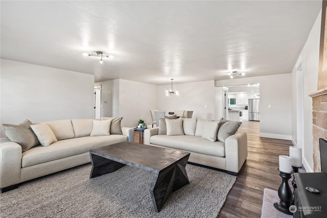 living room with a stone fireplace, dark wood-type flooring, and a notable chandelier