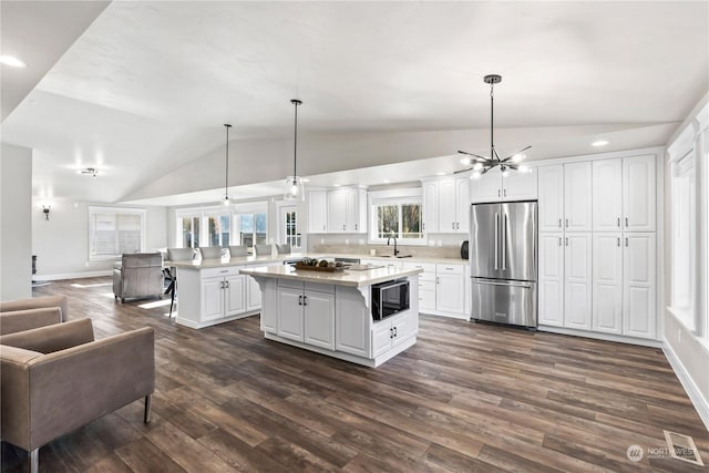 kitchen with decorative light fixtures, stainless steel fridge, white cabinets, and a kitchen island