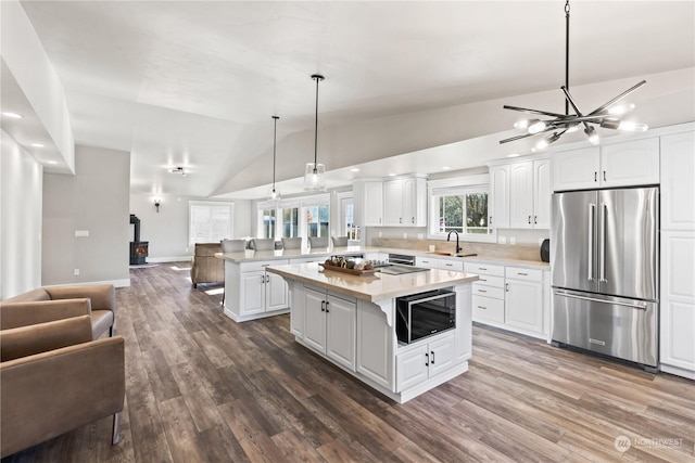 kitchen with high end fridge, built in microwave, lofted ceiling, and white cabinetry