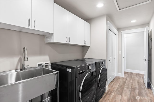 clothes washing area featuring cabinets, sink, washing machine and clothes dryer, and light hardwood / wood-style floors