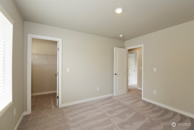 unfurnished bedroom with a walk in closet, light colored carpet, and a closet