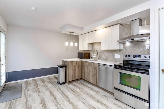 kitchen featuring pendant lighting, wall chimney range hood, sink, appliances with stainless steel finishes, and tasteful backsplash