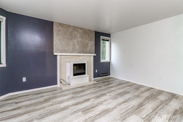unfurnished living room with a baseboard heating unit, a large fireplace, and light wood-type flooring