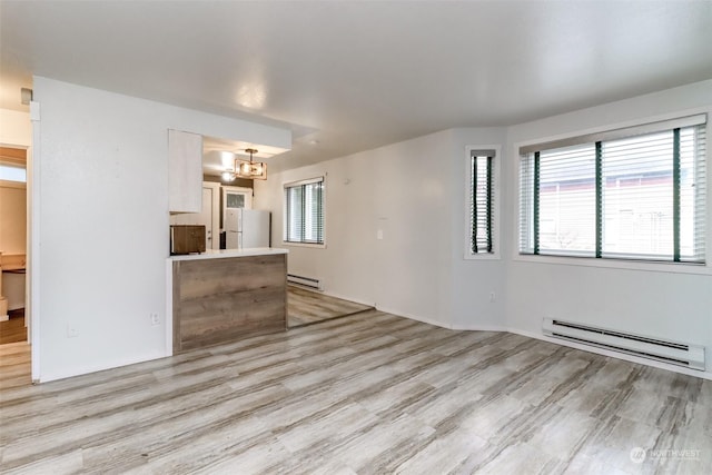 unfurnished living room featuring an inviting chandelier, a baseboard radiator, and light hardwood / wood-style flooring