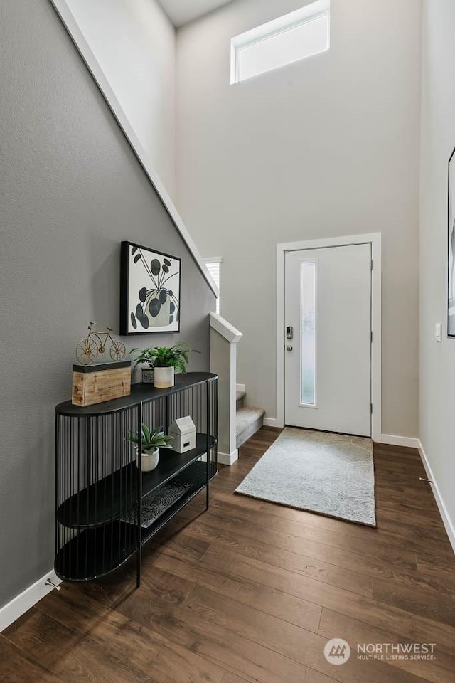 foyer entrance featuring baseboards, stairs, a high ceiling, and dark wood-style flooring