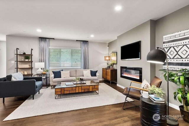 living room featuring dark wood-style flooring, recessed lighting, a glass covered fireplace, and baseboards