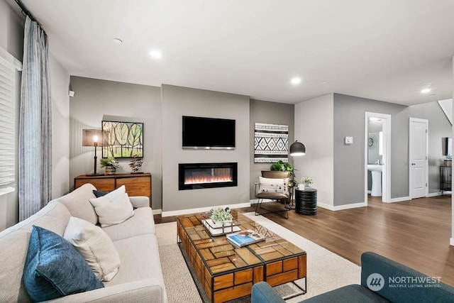 living area with wood finished floors, recessed lighting, a glass covered fireplace, and baseboards