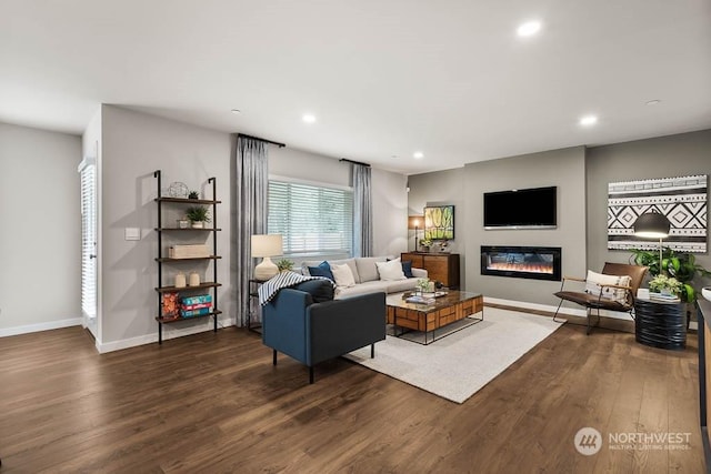 living area with dark wood-type flooring, a glass covered fireplace, baseboards, and recessed lighting