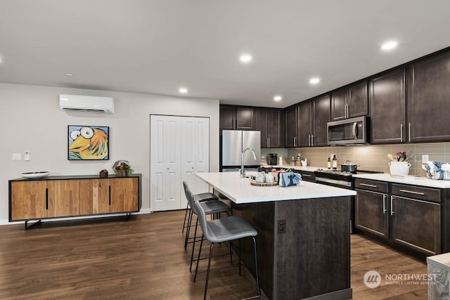 kitchen with a wall unit AC, a center island with sink, a breakfast bar area, light countertops, and appliances with stainless steel finishes