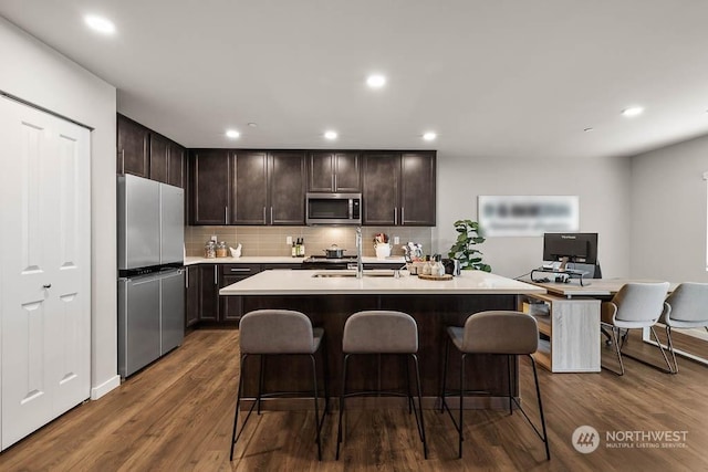 kitchen featuring sink, a breakfast bar, appliances with stainless steel finishes, a kitchen island with sink, and dark hardwood / wood-style flooring