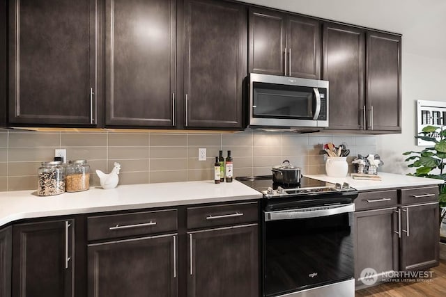 kitchen featuring electric range oven, backsplash, dark brown cabinets, and wood-type flooring