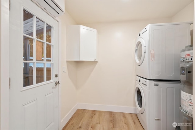 clothes washing area with stacked washer / dryer, light wood-type flooring, a wall mounted AC, and cabinets