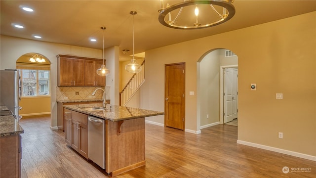 kitchen featuring sink, a kitchen island with sink, hanging light fixtures, stainless steel appliances, and tasteful backsplash