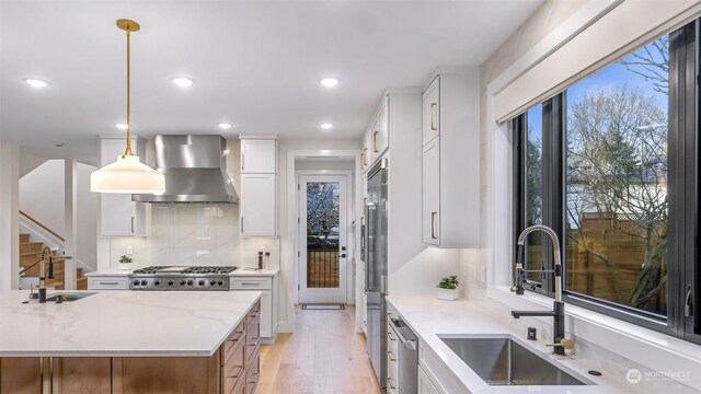 kitchen with wall chimney exhaust hood, sink, pendant lighting, light stone countertops, and white cabinets