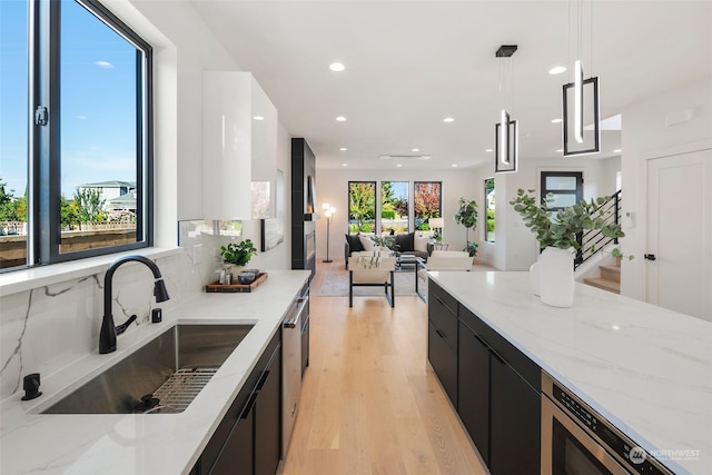 kitchen featuring sink, light hardwood / wood-style flooring, hanging light fixtures, stainless steel appliances, and light stone counters