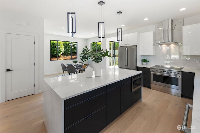 kitchen with a kitchen island, white cabinetry, hanging light fixtures, high end appliances, and wall chimney range hood