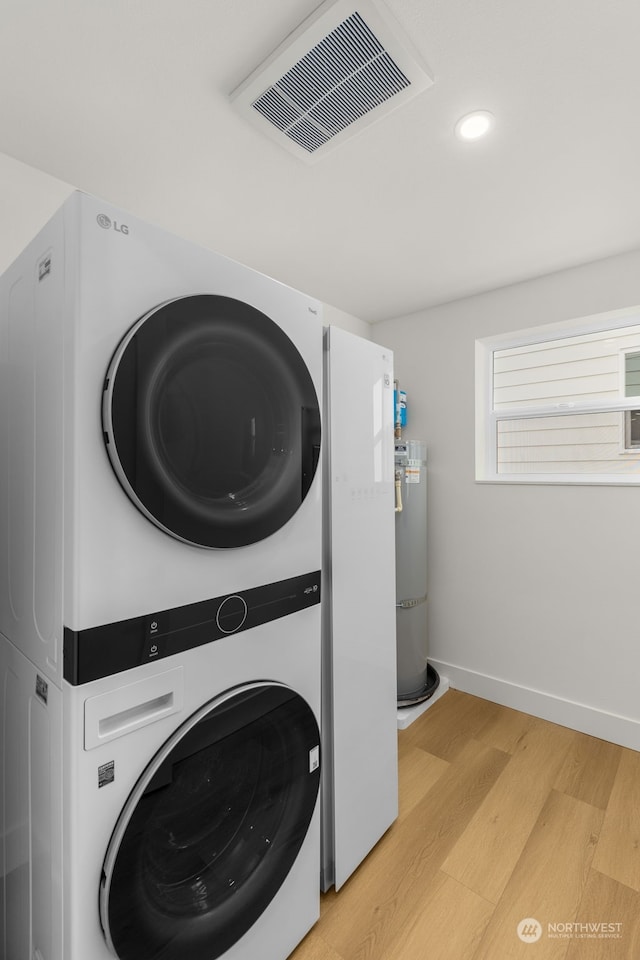 laundry room featuring stacked washer and dryer, water heater, and light hardwood / wood-style flooring