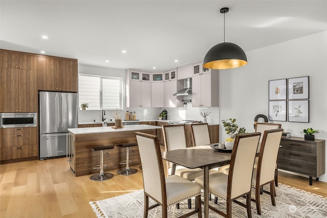 kitchen featuring white cabinetry, tasteful backsplash, decorative light fixtures, appliances with stainless steel finishes, and wall chimney range hood