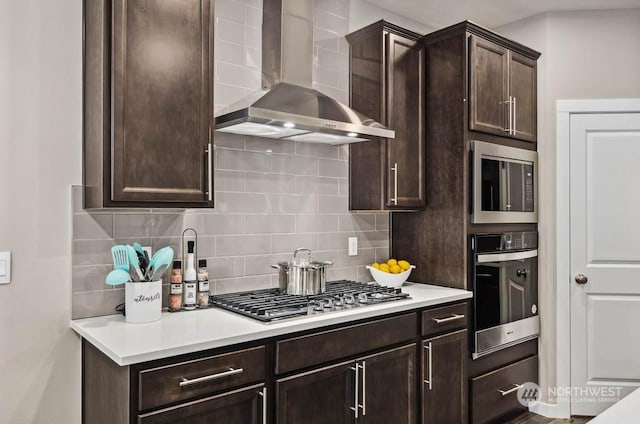 kitchen featuring dark brown cabinets, stainless steel appliances, decorative backsplash, and wall chimney range hood