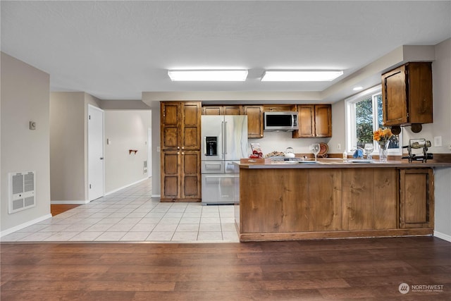 kitchen with heating unit, stainless steel appliances, light hardwood / wood-style floors, and kitchen peninsula