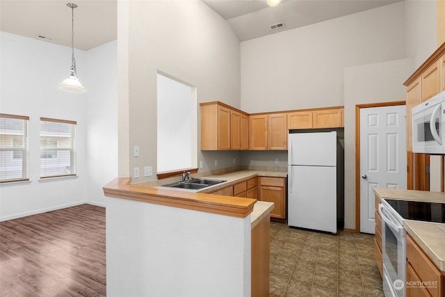 kitchen with sink, kitchen peninsula, pendant lighting, white appliances, and a high ceiling