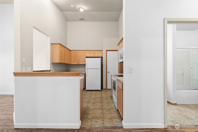 kitchen featuring a high ceiling, light brown cabinets, and white appliances