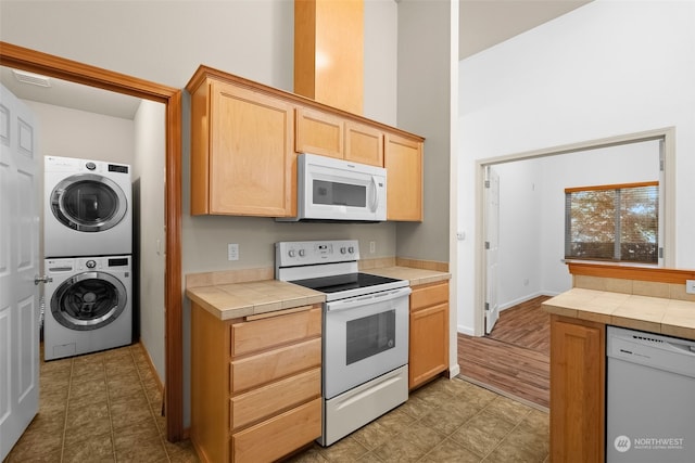 kitchen featuring light brown cabinetry, white appliances, tile counters, and stacked washer and clothes dryer