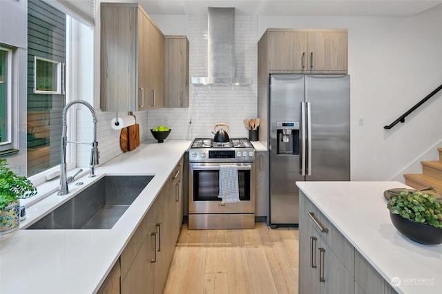 kitchen featuring sink, stainless steel appliances, light hardwood / wood-style floors, decorative backsplash, and wall chimney range hood