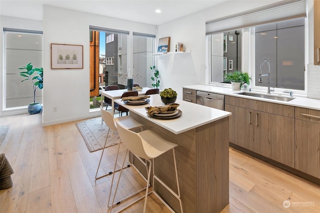 kitchen with a kitchen bar, sink, light wood-type flooring, stainless steel dishwasher, and a kitchen island