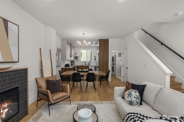 living room with a chandelier, stacked washer and dryer, a tiled fireplace, and light hardwood / wood-style floors