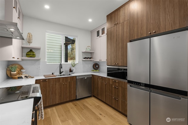 kitchen featuring extractor fan, appliances with stainless steel finishes, tasteful backsplash, sink, and light hardwood / wood-style flooring