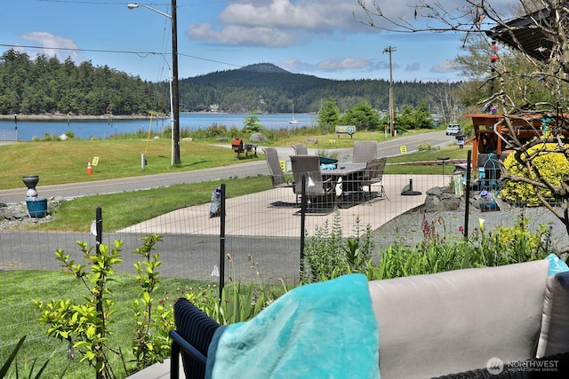 view of patio featuring a wooded view, a water view, and fence