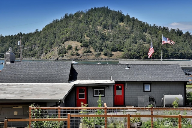 view of front of property featuring a water view, fence, a wooded view, a shingled roof, and a chimney