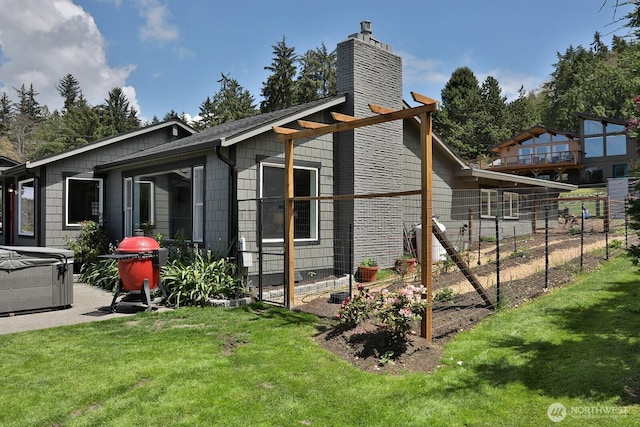 view of side of property with fence, a garden, a chimney, a hot tub, and a lawn