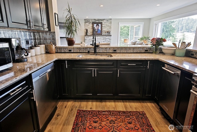 kitchen featuring appliances with stainless steel finishes, dark cabinetry, light wood-style floors, and a sink