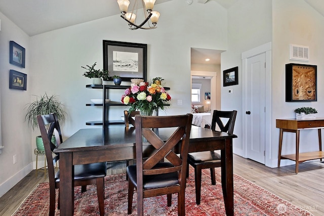 dining area featuring wood finished floors, visible vents, baseboards, an inviting chandelier, and lofted ceiling