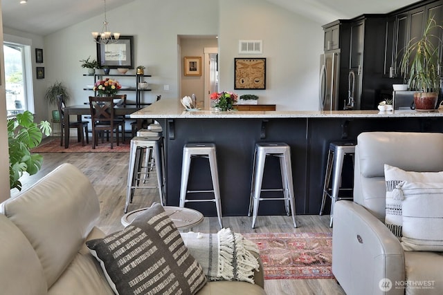 kitchen featuring light stone counters, visible vents, freestanding refrigerator, and lofted ceiling