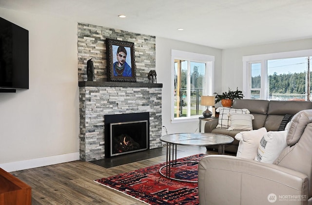 living area with recessed lighting, baseboards, a stone fireplace, and wood finished floors