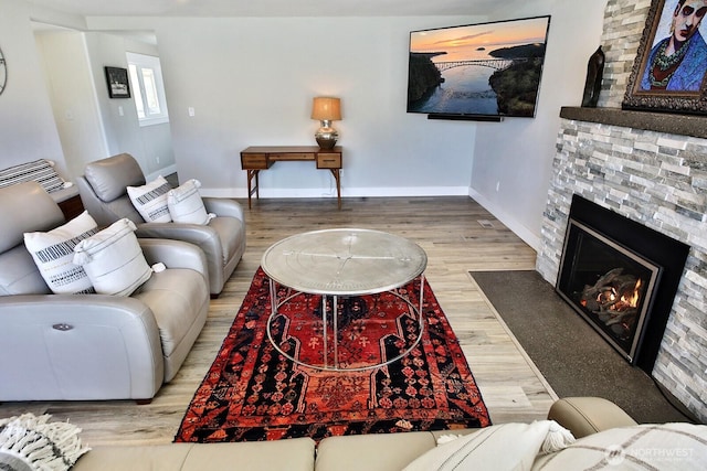 living room featuring a stone fireplace, baseboards, and wood finished floors