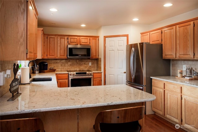 kitchen with stainless steel appliances, sink, light stone counters, and kitchen peninsula