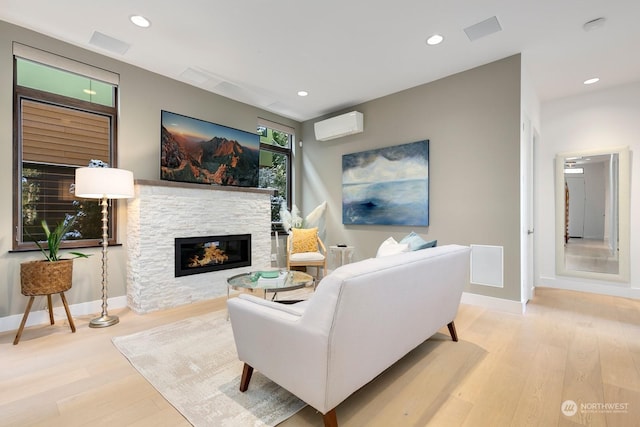 living room with a stone fireplace, a wall unit AC, and light hardwood / wood-style floors