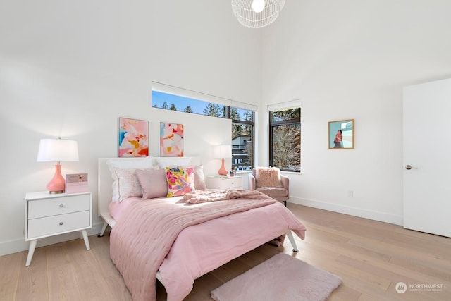 bedroom with a towering ceiling and light hardwood / wood-style floors