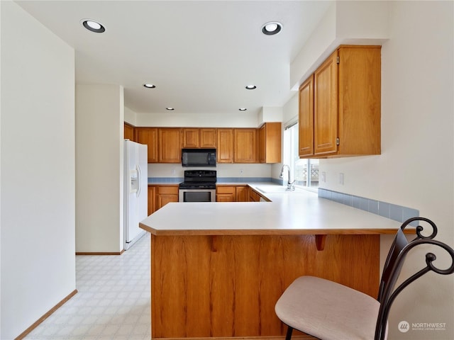 kitchen with sink, a breakfast bar area, white fridge with ice dispenser, stainless steel range with electric cooktop, and kitchen peninsula