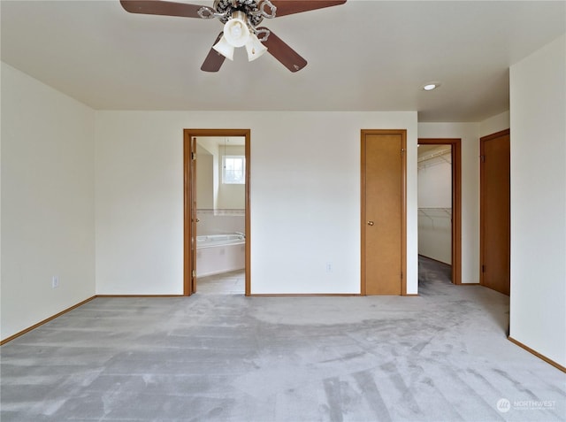 unfurnished bedroom featuring a spacious closet, light colored carpet, ceiling fan, ensuite bath, and a closet