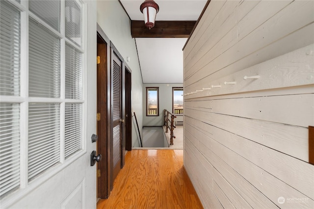 hall featuring light hardwood / wood-style flooring, vaulted ceiling with beams, and wooden walls