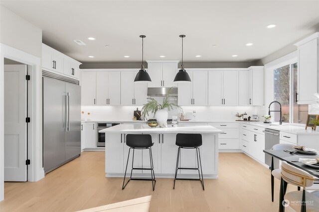 kitchen with a kitchen island, white cabinets, hanging light fixtures, light hardwood / wood-style floors, and stainless steel appliances