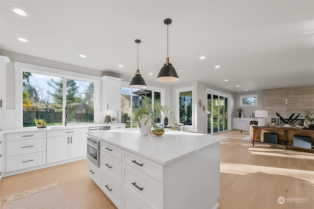 kitchen with sink, white cabinetry, hanging light fixtures, a kitchen island, and light hardwood / wood-style floors