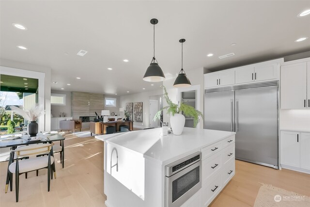 kitchen with a kitchen island, decorative light fixtures, white cabinets, built in appliances, and light wood-type flooring