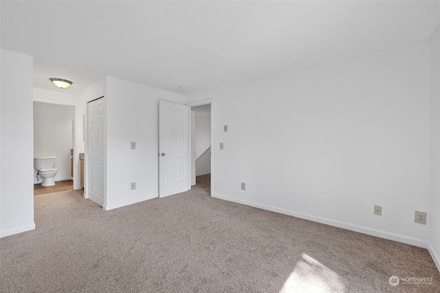 unfurnished bedroom with ensuite bath, light colored carpet, and a closet